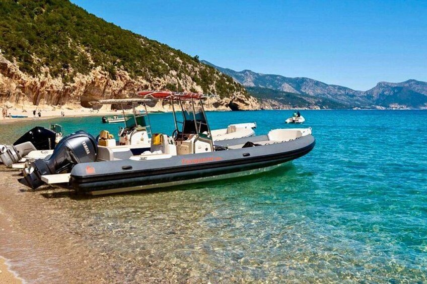 Een kleine motorboot ligt aangemeerd op een helder turquoise strand, met rotsachtige kliffen op de achtergrond. 3