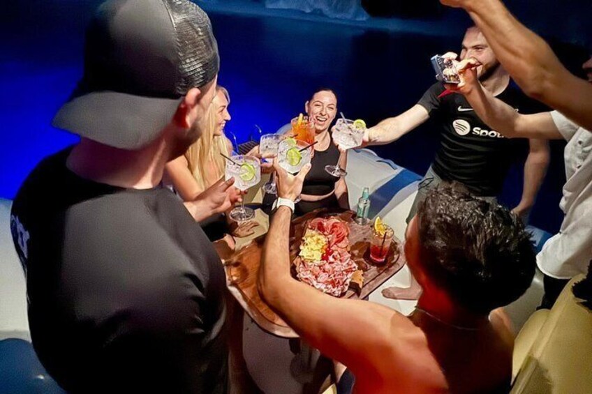 A group of people toasting with drinks around a table with food. 2