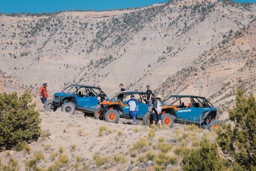 Off-road vehicles parked on a desert terrain with people standing around them. 5