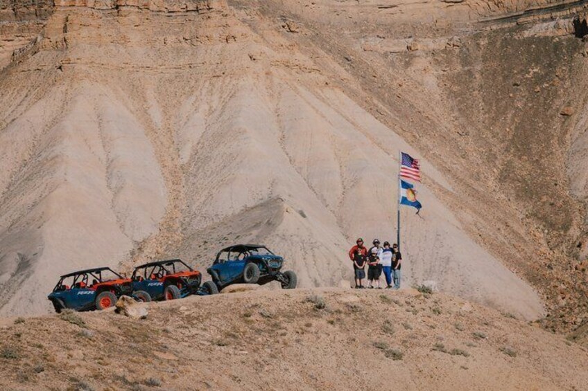 Off-road vehicles on a sandy terrain with a flag and people in the background. 4