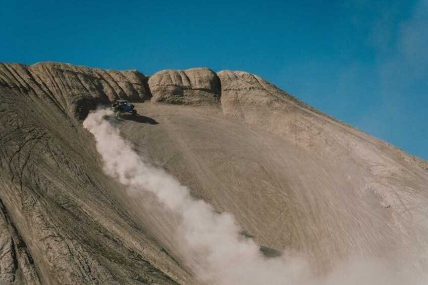 A vehicle descending a steep, rocky slope with dust trailing behind. 2