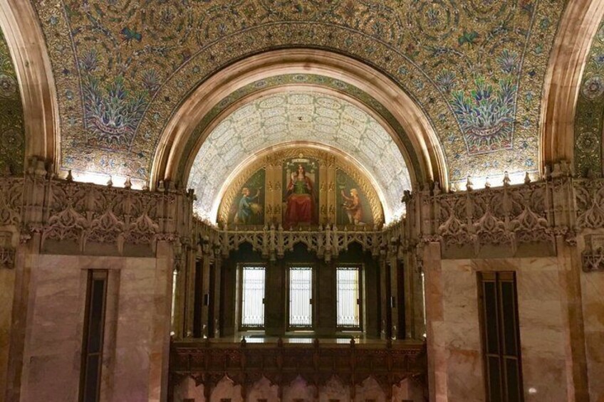 An ornate interior with a detailed ceiling, a large arched window, and classical columns. 1