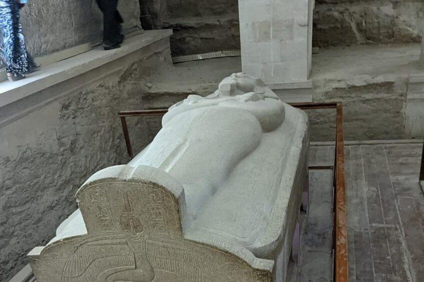 A sarcophagus with hieroglyphics, a stone wall, and a window with a decorative vase. 5