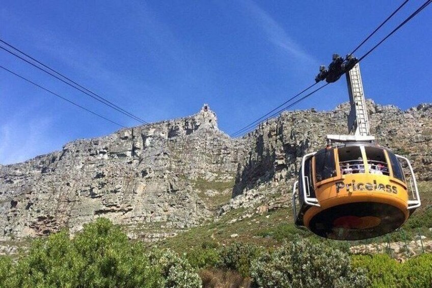A cable car with 'Priceiss' written on it, suspended above a rocky mountain landscape. 1