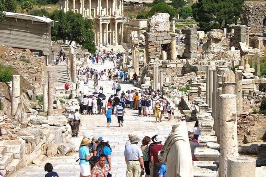 Ancient ruins with columns and stone structures, a crowd of people, and a building in the background. 2