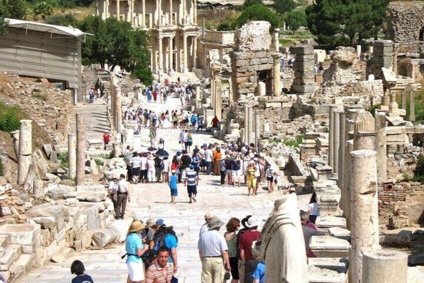 Ancient ruins with columns and stone structures, a crowd of visitors, and a hillside in the background. 2