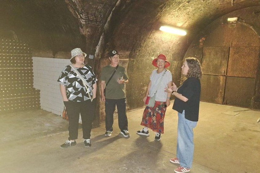Four people standing in a dimly lit, arched tunnel with concrete walls and a white fence on the left. 4
