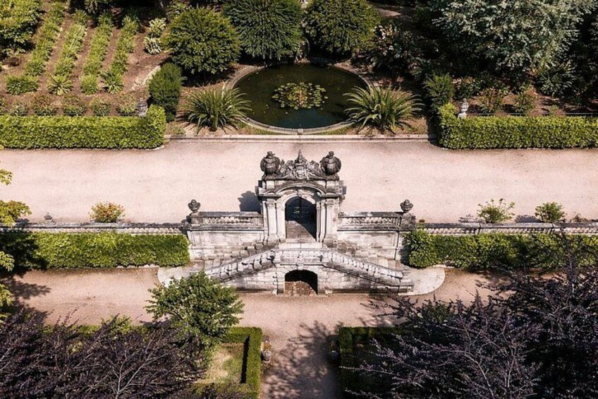An aerial view of a historic gate with a staircase leading up to it, surrounded by well-maintained gardens and a pond. 2