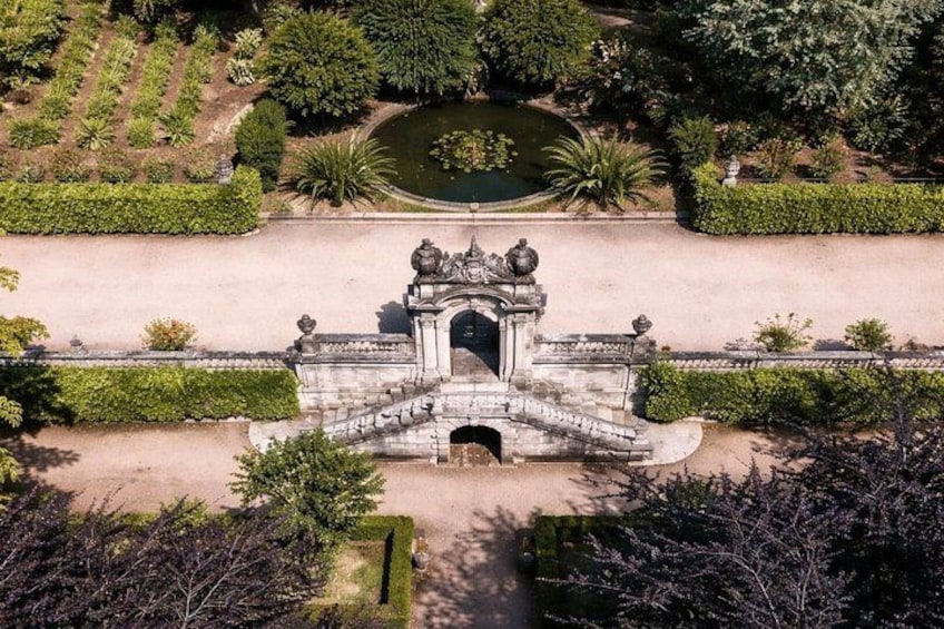 An aerial view of a historic gate with intricate carvings, surrounded by well-manicured gardens and a pond. 2