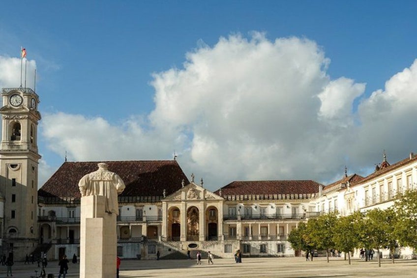 A historic square with a prominent clock tower, a statue, and classical architecture. 4