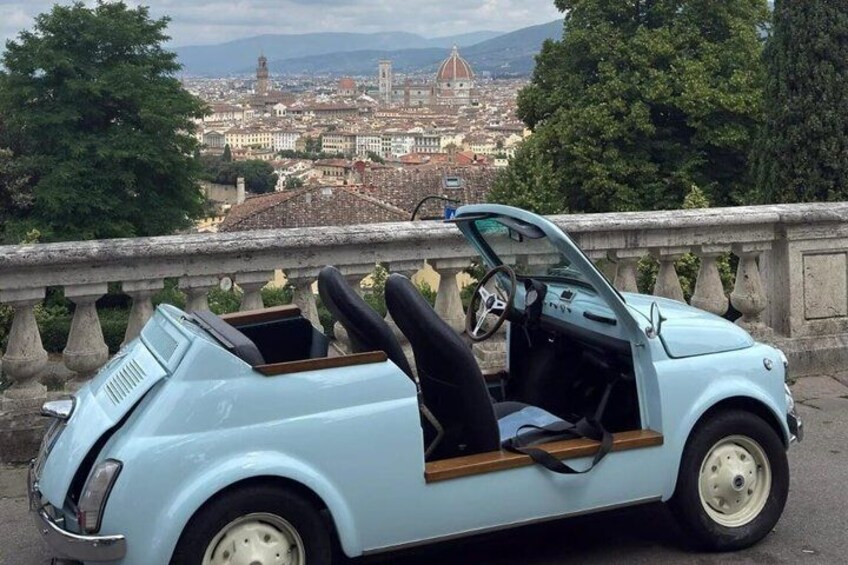 A light blue vintage convertible car parked on a stone bridge with a cityscape in the background. 3