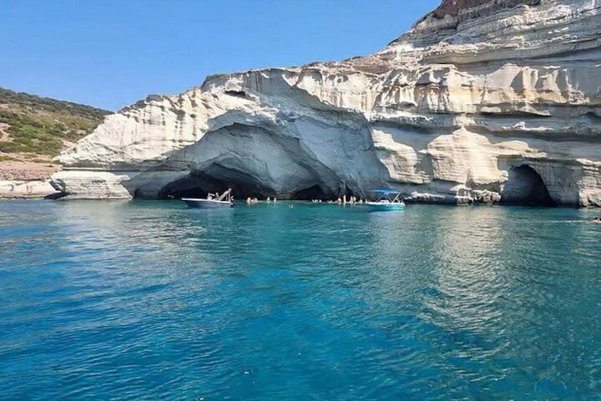 A coastal cave entrance with clear blue water, a boat, and rocky cliffs. 1