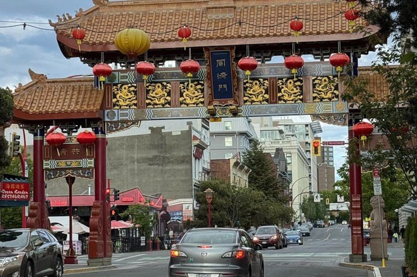 A traditional Chinese gate with red lanterns, a sign for a restaurant, and cars on the street. 2