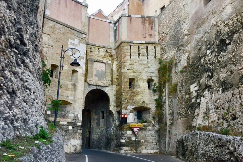 A narrow medieval stone archway with a street lamp and a triangular warning sign. 2