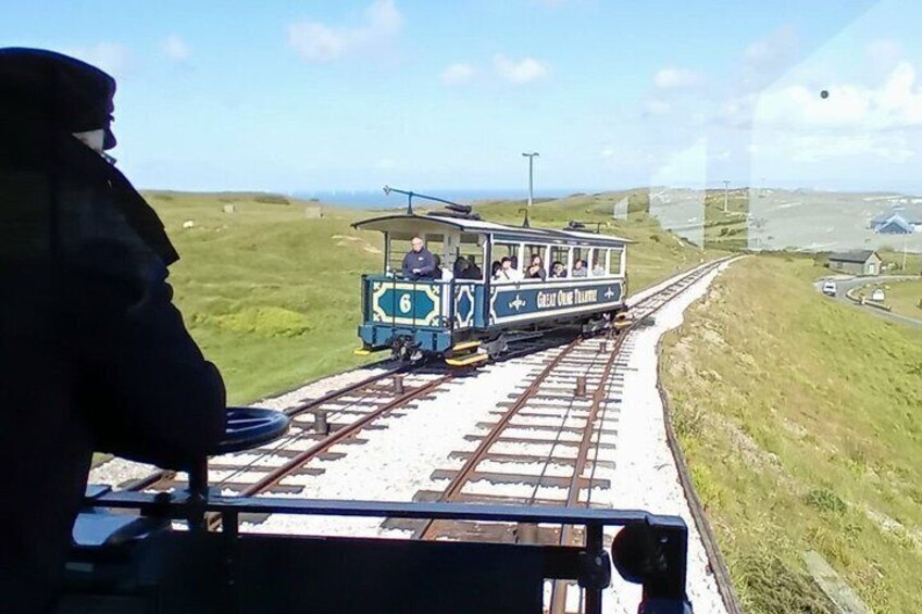 A small train on tracks with passengers, a grassy landscape, and a clear sky. 3