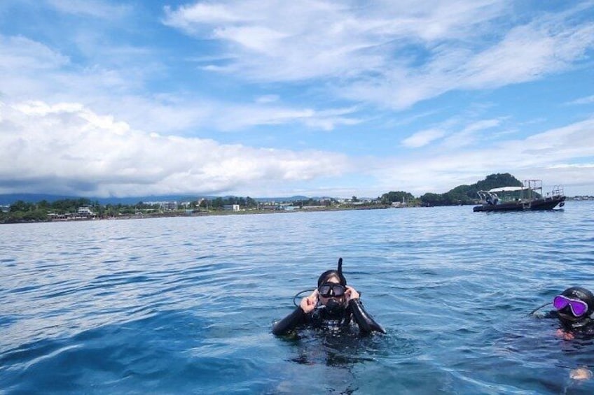 Two people snorkeling in clear blue water with a boat and a distant shoreline in the background. 2