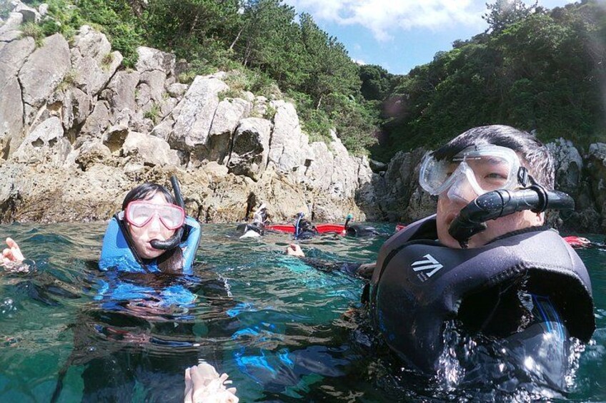 Two people snorkeling in clear water with rocky cliffs in the background. 3