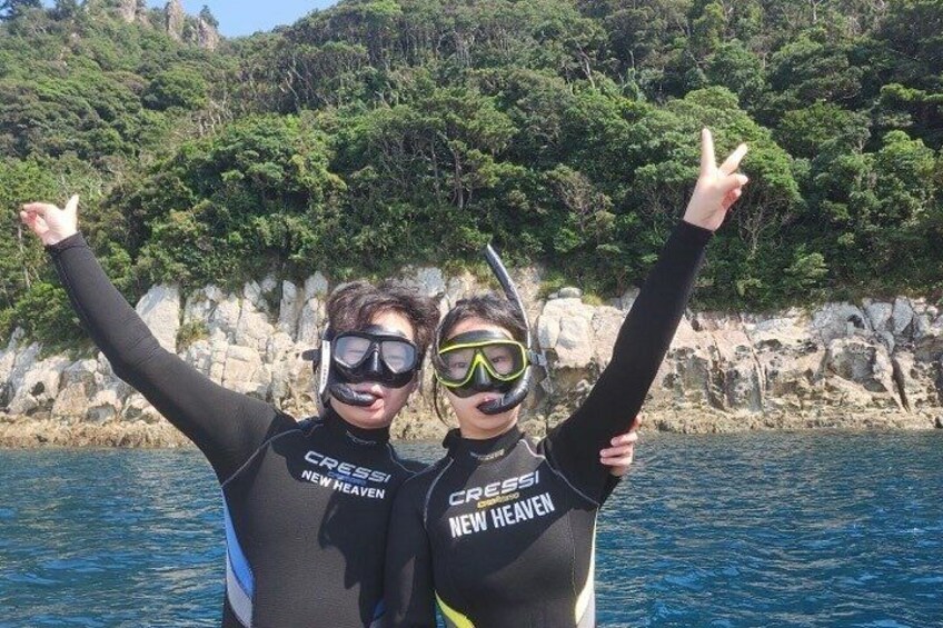 Two people in wetsuits with 'CRESSI NEW HEAVEN' on them, standing on a boat with a rocky coastline and greenery in the background. 4