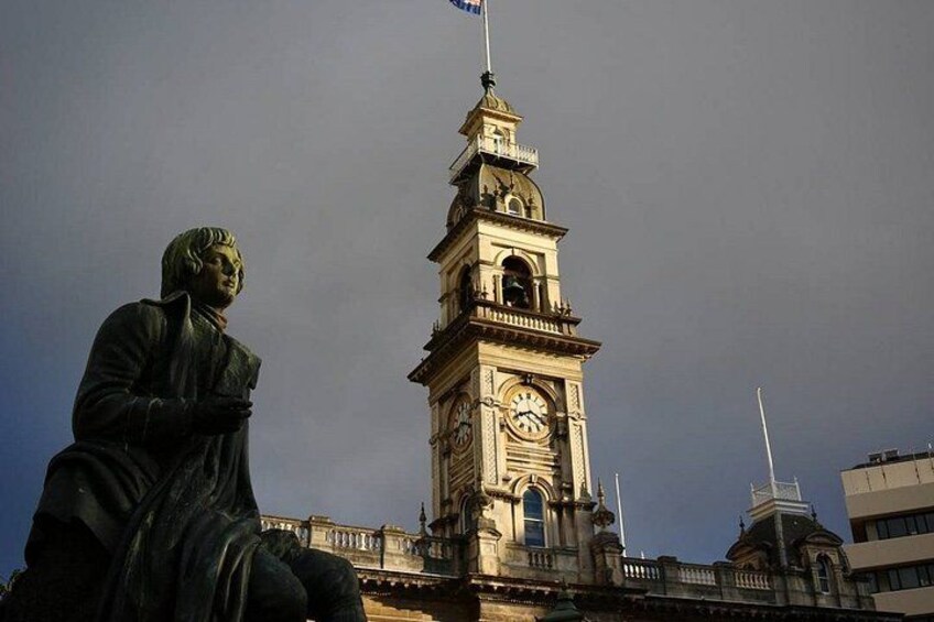 A statue of a man, a clock tower, and a building with a flag. 2
