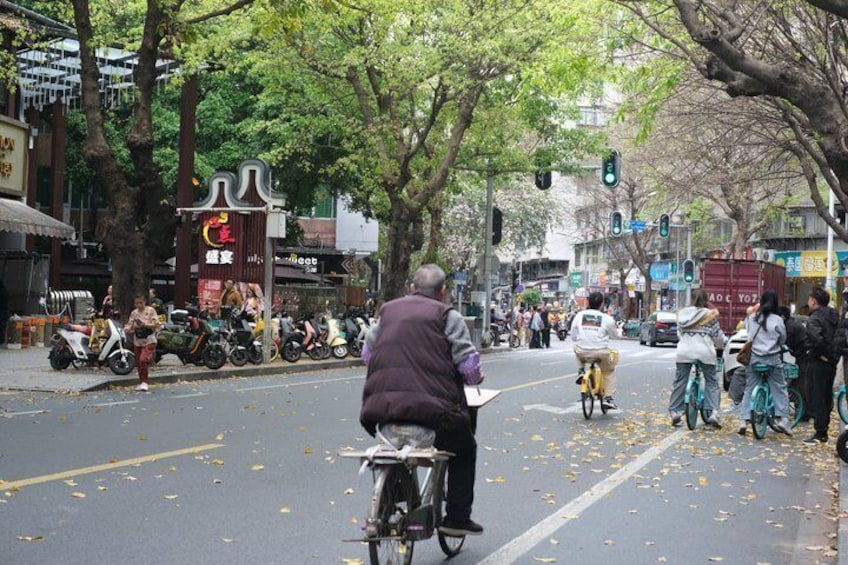 A street scene with a man on a bicycle, parked scooters, and pedestrians. 2