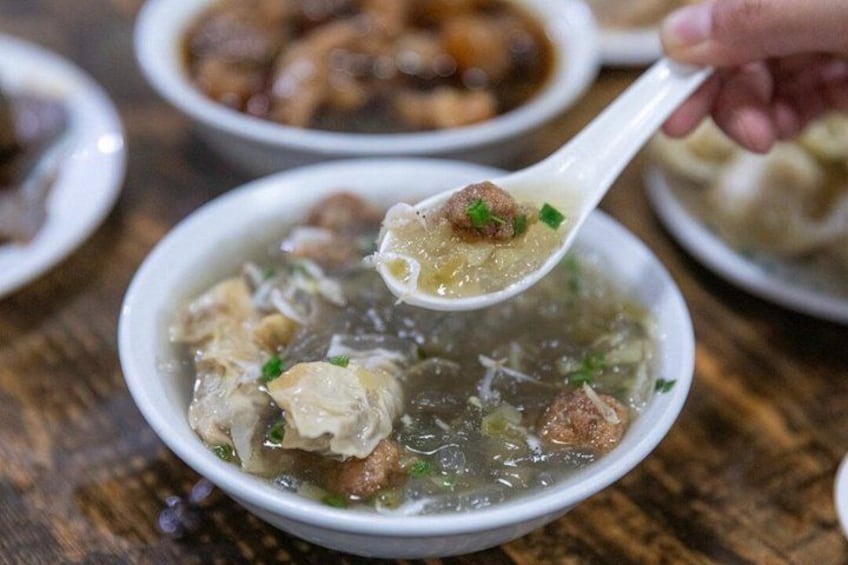 A bowl of soup with dumplings and meatballs, garnished with green herbs. 2