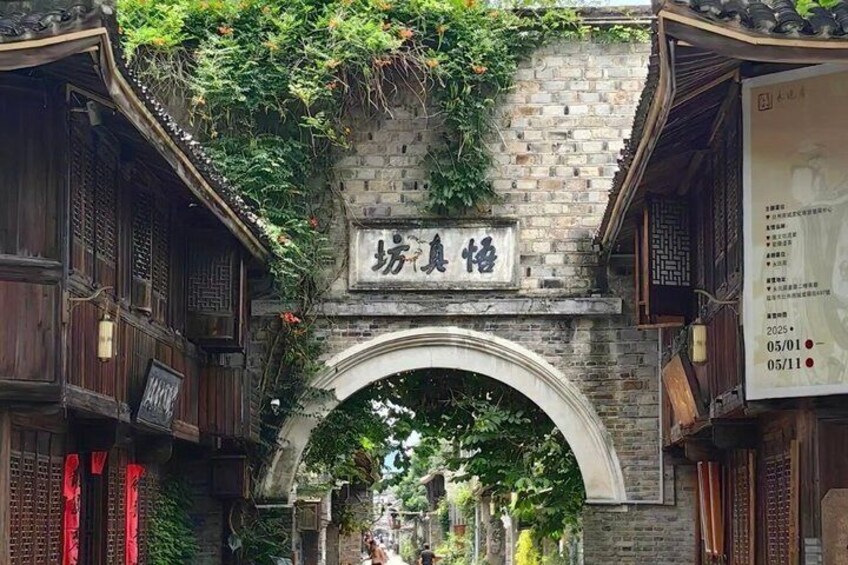A traditional wooden archway with a sign above it, surrounded by greenery and buildings. 5