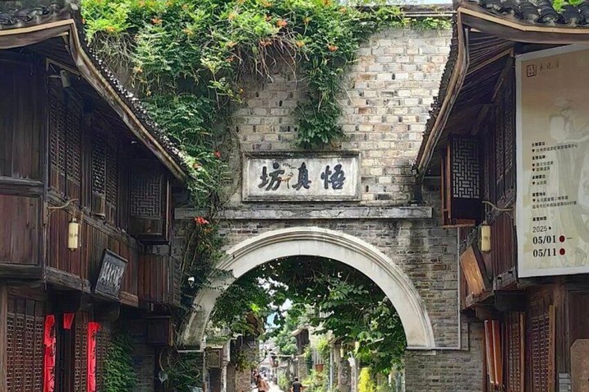 A traditional Chinese archway with a sign, surrounded by lush greenery and wooden buildings. 5