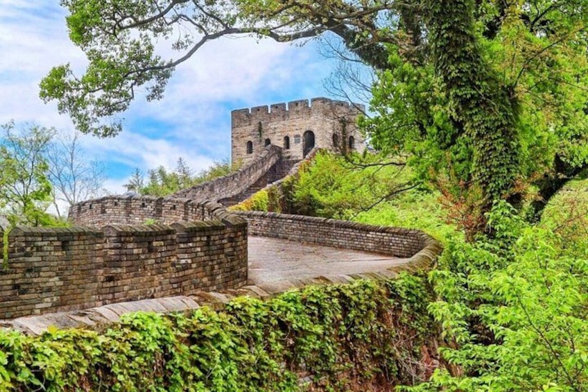 A historic stone wall with a watchtower, surrounded by lush greenery. 1
