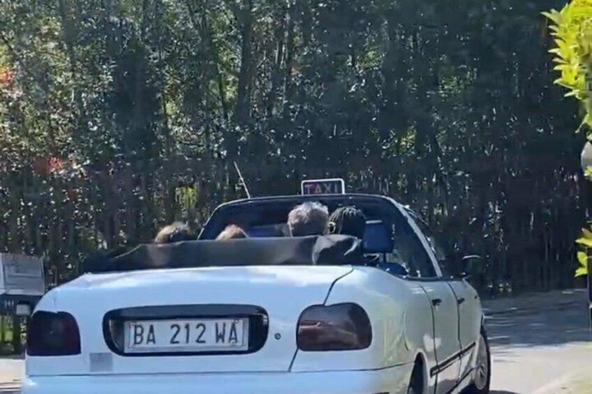 A white convertible taxi with a 'TAXI' sign on top, a visible license plate 'BA 212 WA', and passengers inside. 3