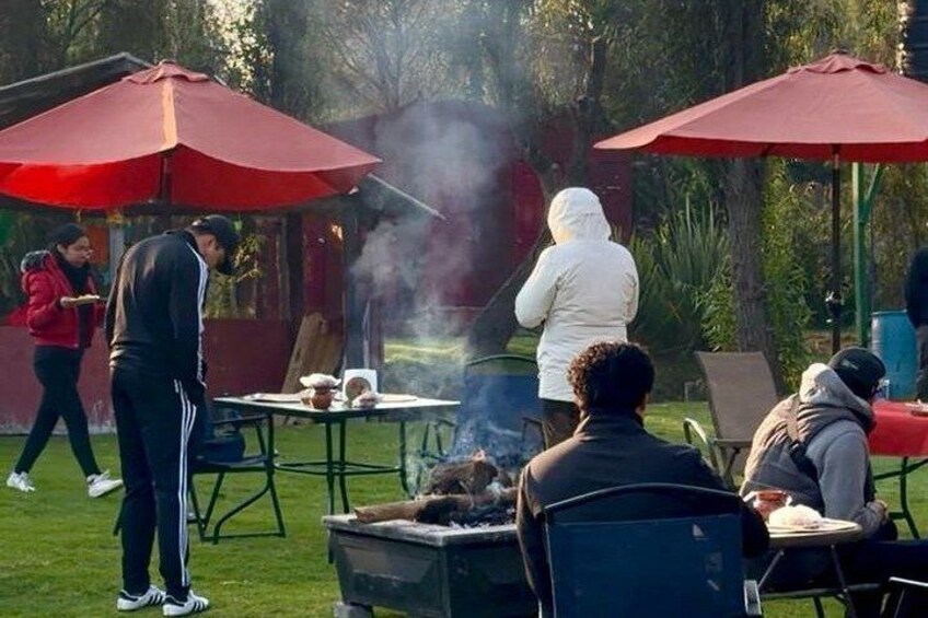 People gathered around a barbecue grill outdoors with tables and umbrellas. 5