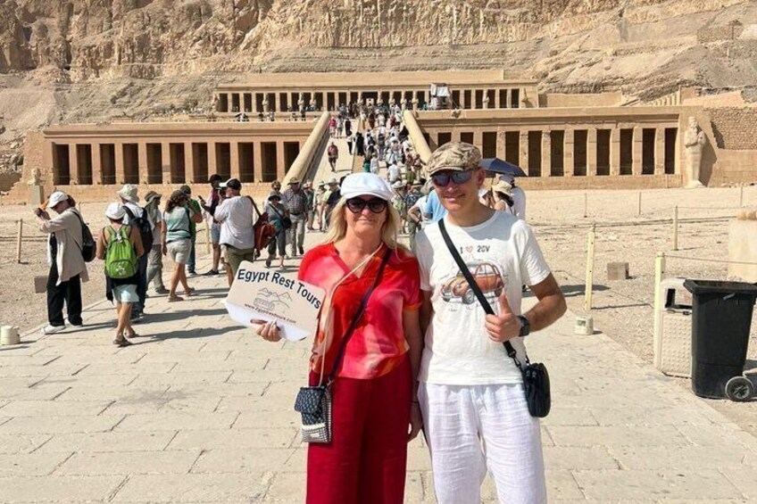 Tourists at the entrance of a large ancient Egyptian temple with hieroglyphics and a grand staircase leading up to the temple. 1