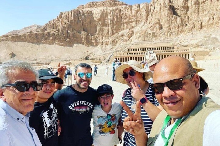 A group of people in a desert landscape with rocky formations and a large building in the background. 1