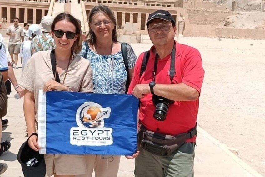 A person holding a flag with 'EGYPT REST TOURS' text, another person with a camera, and a historical site in the background. 5