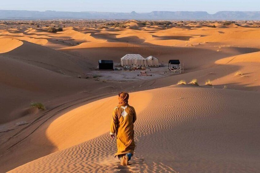 A person walking on a sand dune with tents in the background. 4