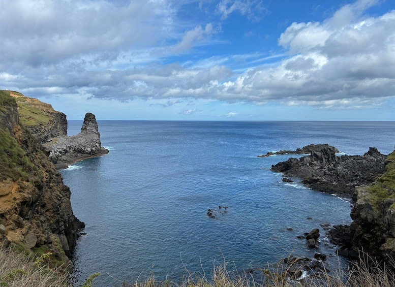 A coastal landscape with rocky cliffs and a clear blue sea under a partly cloudy sky. 2