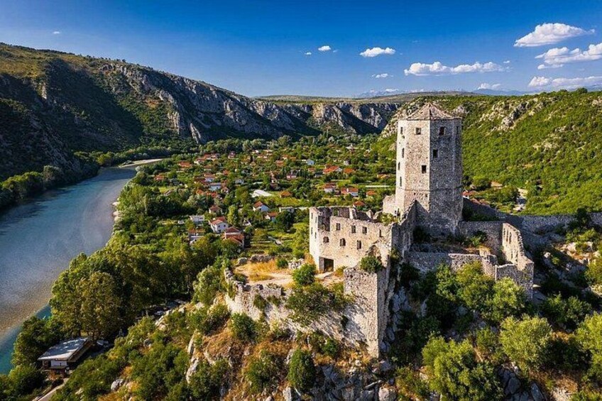 A historic castle on a cliff overlooking a river, surrounded by lush greenery and a mountainous landscape. 2