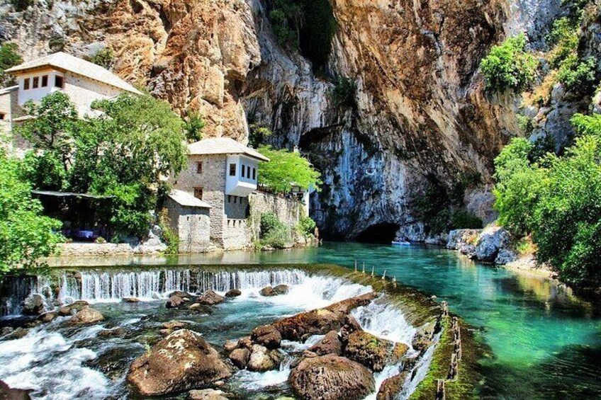 A river with a waterfall, rocky cliffs, and buildings near the water. 3
