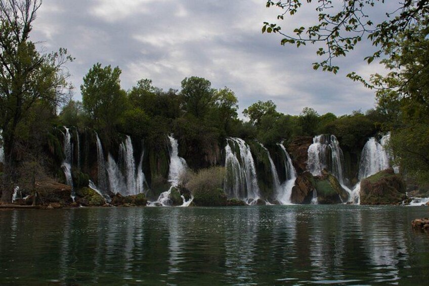 A series of waterfalls in a forested area with a body of water in the foreground. 5