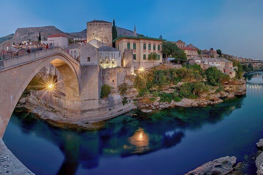 A stone bridge over a calm river, historic buildings, and a clear night sky. 1
