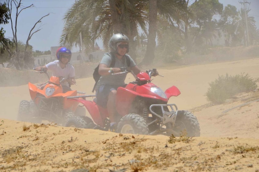Two people riding off-road vehicles on a sandy terrain with palm trees in the background. 2
