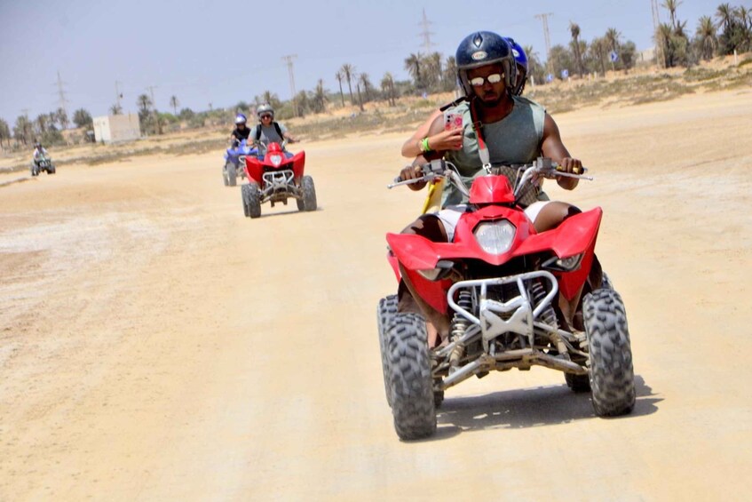 A person riding a red quad bike on a sandy road with palm trees in the background. 5
