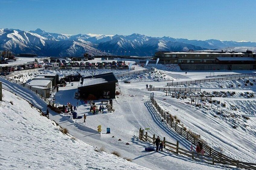 A snowy ski resort with a ski lift, buildings, and mountains in the background. 2