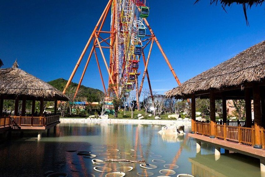 A Ferris wheel, a water body, and thatched-roof structures. 2