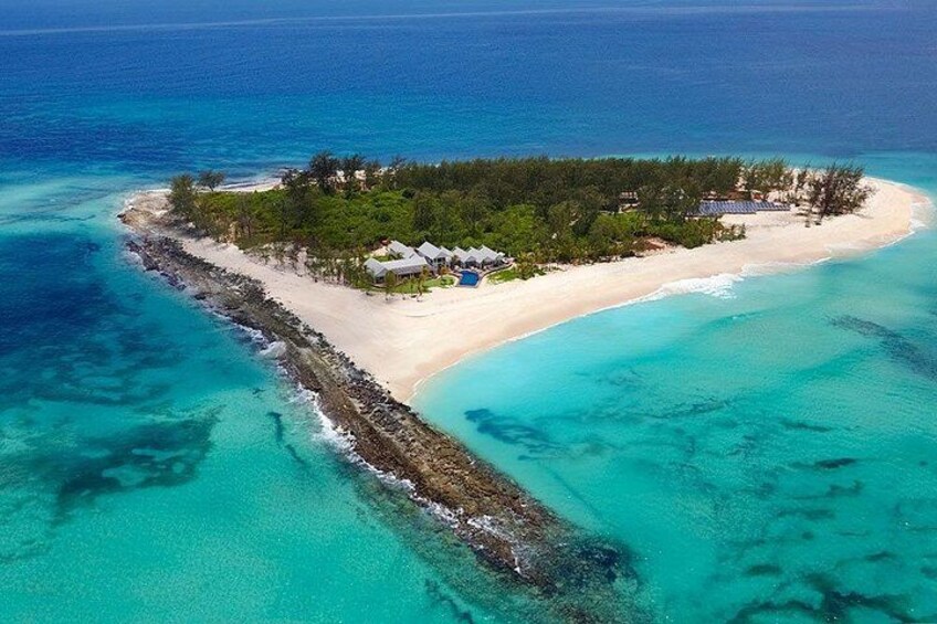 A tropical island with a beach, clear turquoise waters, and a rocky shoreline. 5