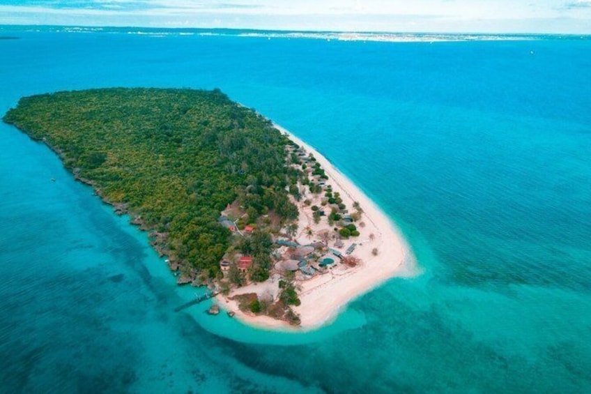 An aerial view of a tropical island with clear turquoise waters, dense green vegetation, and a small settlement with buildings and a beach. 1