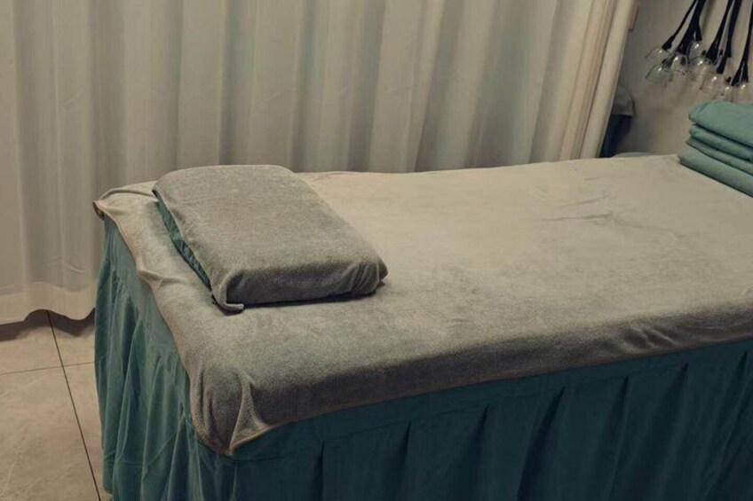 A massage table with a teal bedspread and a single gray pillow. 5
