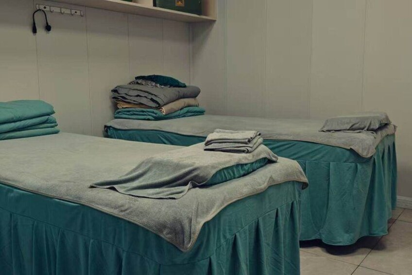 A room with two beds, each covered with teal sheets and blankets, and a shelf with folded clothes. 2