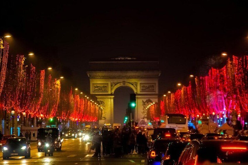 A nighttime view of the Arc de Triomphe with red lights and a busy street. 5
