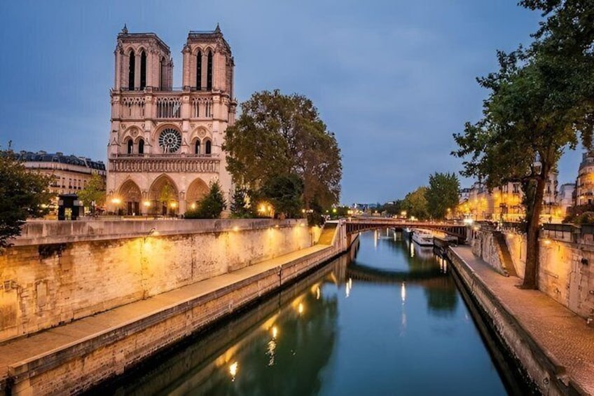 A historic cathedral with twin towers, a calm river, and a tree-lined bridge. 5