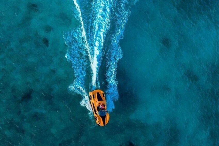An orange boat with a wake, traveling on clear blue water. 3